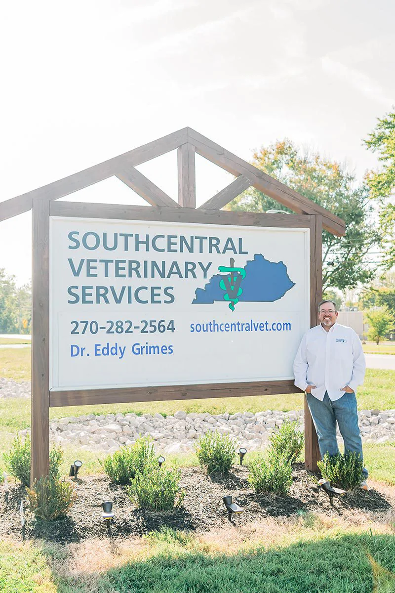 male smiling and standing outside next to sign that says "Southcentral Veterinary Services 270-282-2564 southcentralvet.com Dr. Eddy Grimes"