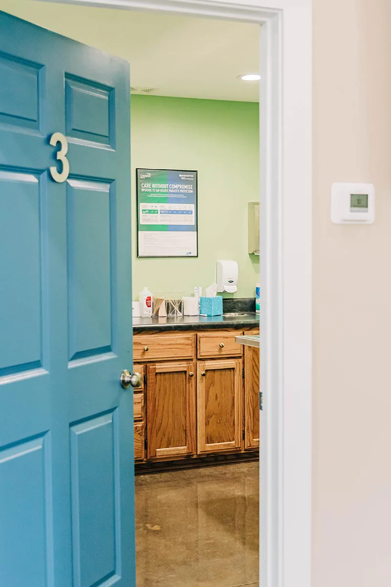 blue door with number 3 on it open ajar to show exam room inside